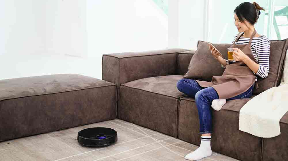 Žena sed&iacute; na pohovce a robotick&yacute; vysavač ukl&iacute;z&iacute;_02
