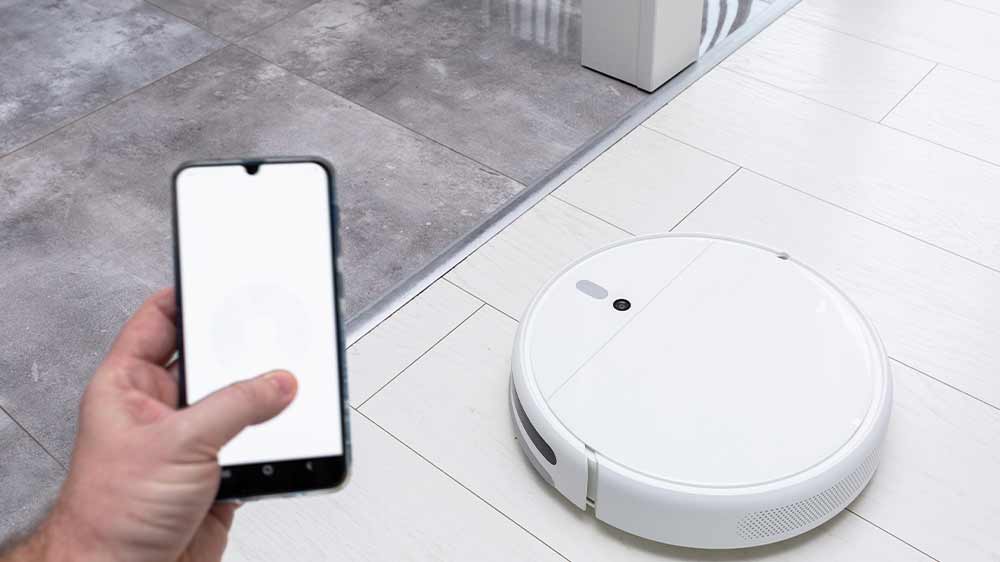 Mužská ruka držící mobilní telefon a ovládající s ním robotický vysavač_06