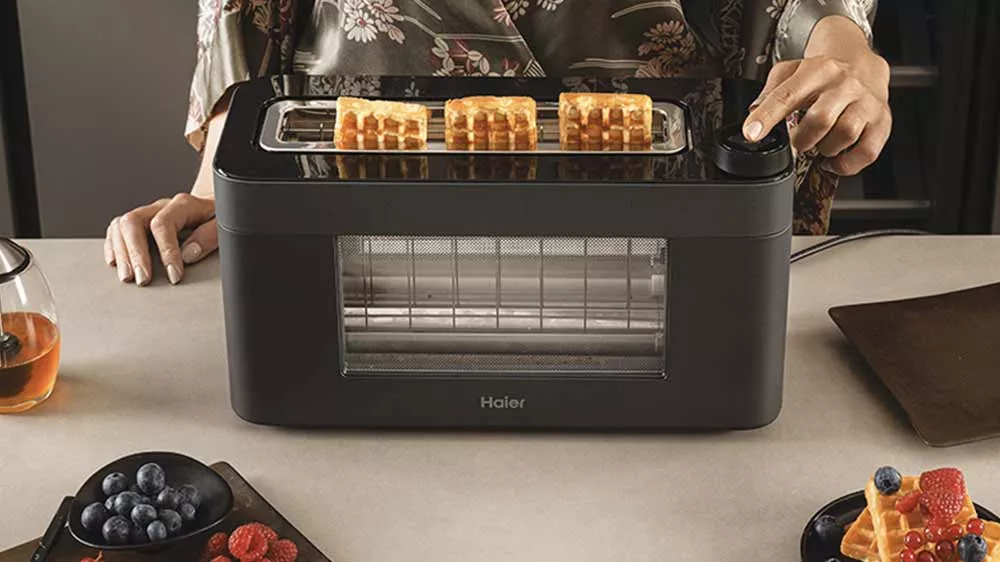 Žensk&aacute; ruka ot&aacute;č&iacute; knofl&iacute;kem na topinkovači Haier HTO7W2 011, ve kter&eacute;m jsou vafle_03
