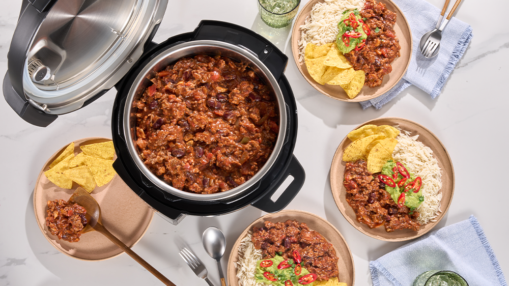 Pohled shora na otevřen&yacute; Instant Pot Classic 5,7 l pln&yacute; j&iacute;dla položen&yacute; na stole spolu s tal&iacute;ři