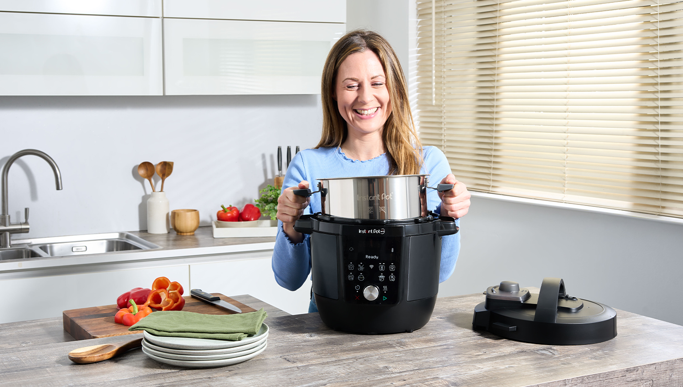 Žena se usmívá a vyndává vnitřní nerezovou nádobu z multifunkčního hrnce Instant Pot Plus WiFi 5,7 l