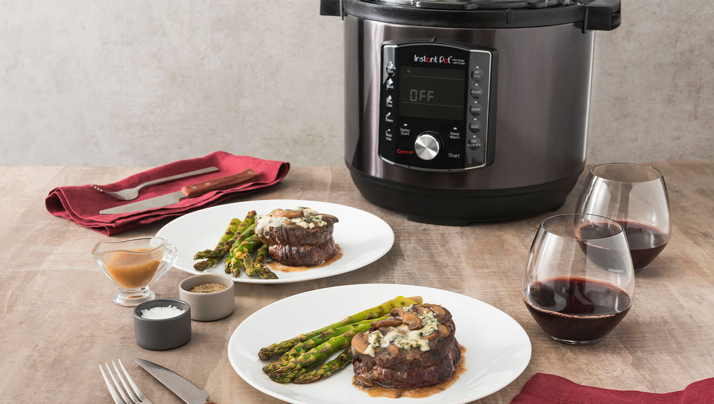 Instant Pot Pro Crisp zobrazený na stole s taniermi s mäsom a špargľou
