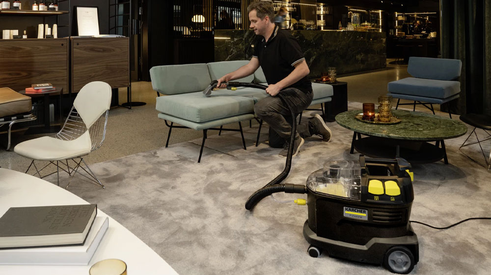 Muž čistící čalouněnou sedačku ve firemních prostorách pomocí extraktoru KÄRCHER Puzzi 8/1 Anniversary Edition_03