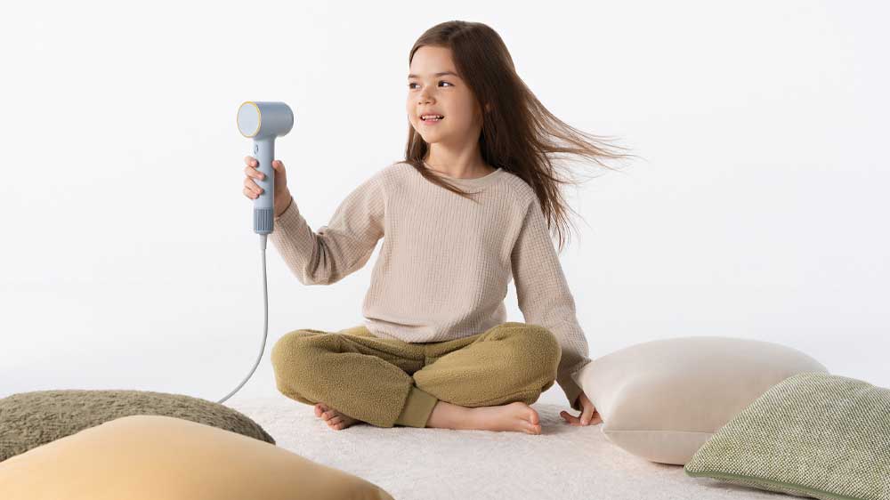 Holčička sedí na koberci a v ruce drží fén_02