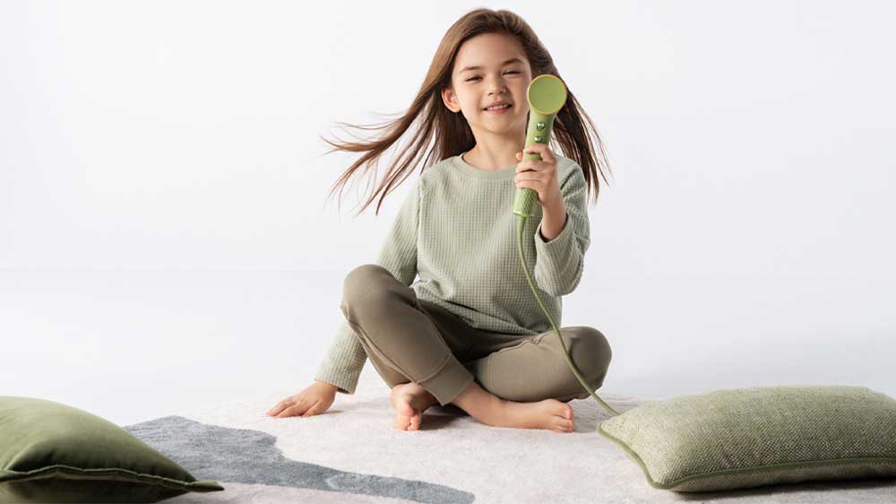 Holčička sedí na koberci a v ruce drží fén_02