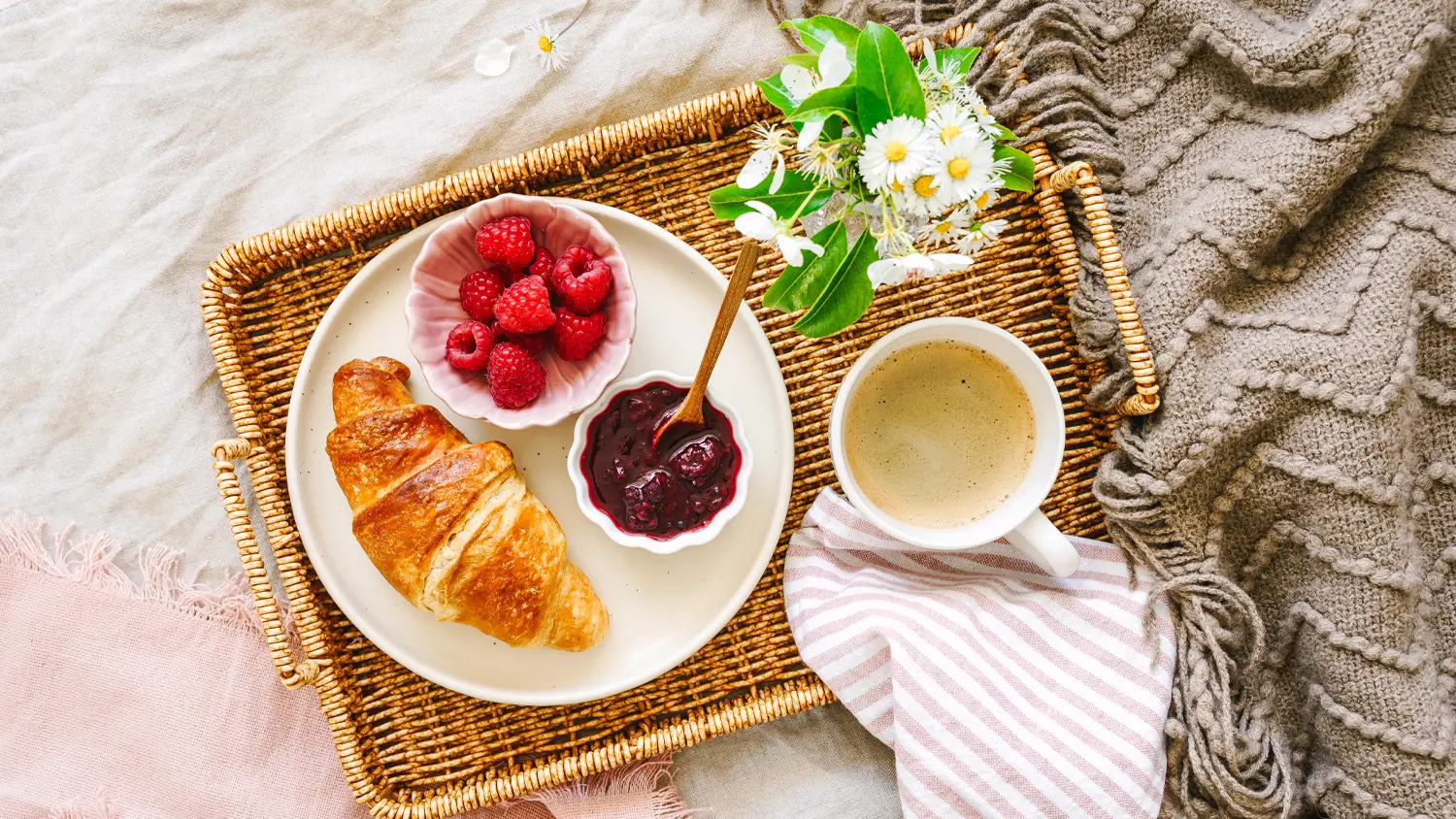 Prútená tácka s kávou a croissantom položená na dekách
