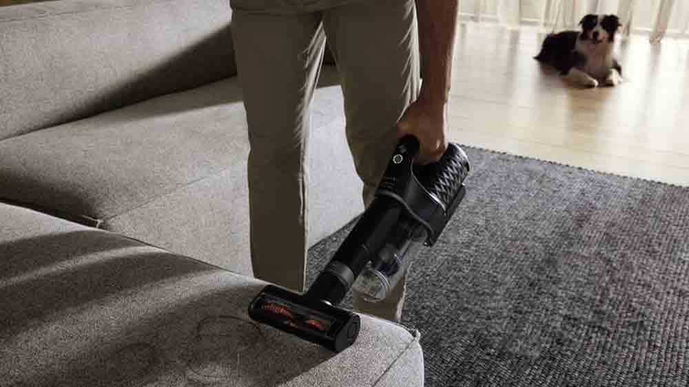 Člověk vys&aacute;v&aacute; chlupy z gauče pomoc&iacute; tyčov&eacute;ho vysavače Miele Duoflex HX1 Cat & Dog_02
