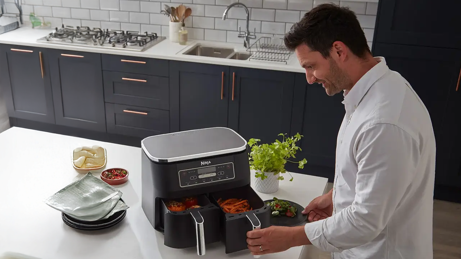 Usměvavá žena dávající na talíř řízky připravené v horkovzdušné fritéze Ninja AF300EU Foodie Dual Zone