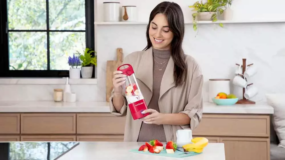 Žena s úsměvem mixuje mléčný koktejl s ovocem ve stolním mixéru Nutribullet NBP003.B_02