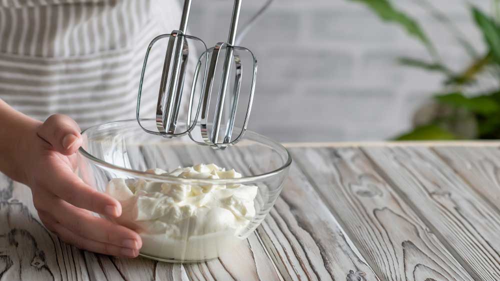 Žena šlehá krém ve skleněné misce ručním šlehačem_02