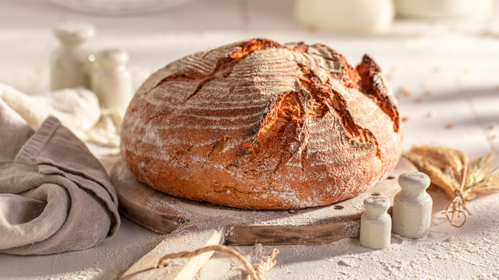Doma upečený kulatý chléb položený na dřevěném prkénku_03
