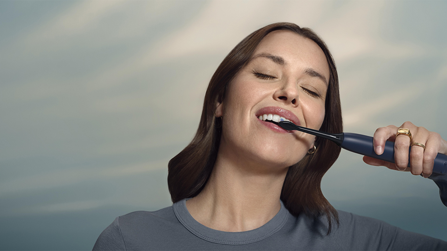 Žena si spokojeně čistí zuby díky Optimal white hlavici a SmarTimer a BrushPacer technologiím