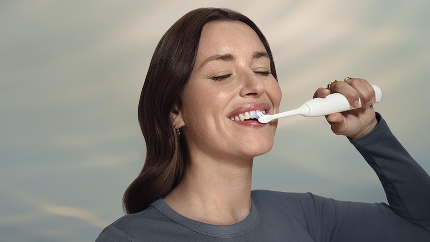 Žena si bezstarostně čistí zuby díky kartáčkové hlavici Sensitive a funkcím SmarTimer a BrushPacer