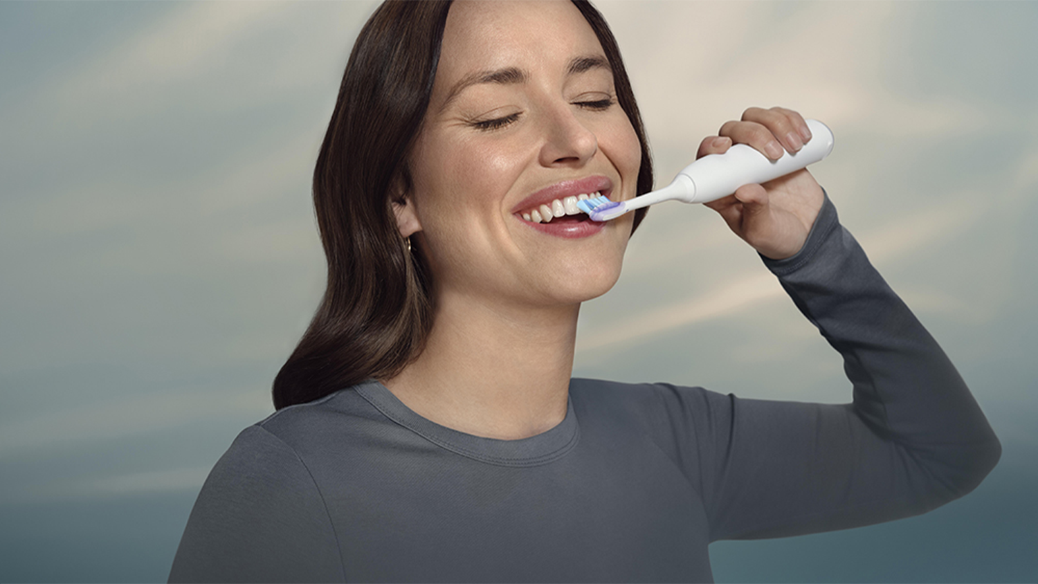 Žena si bezstarostně čistí zuby díky kartáčkové hlavici Sensitive a funkcím SmarTimer a BrushPacer