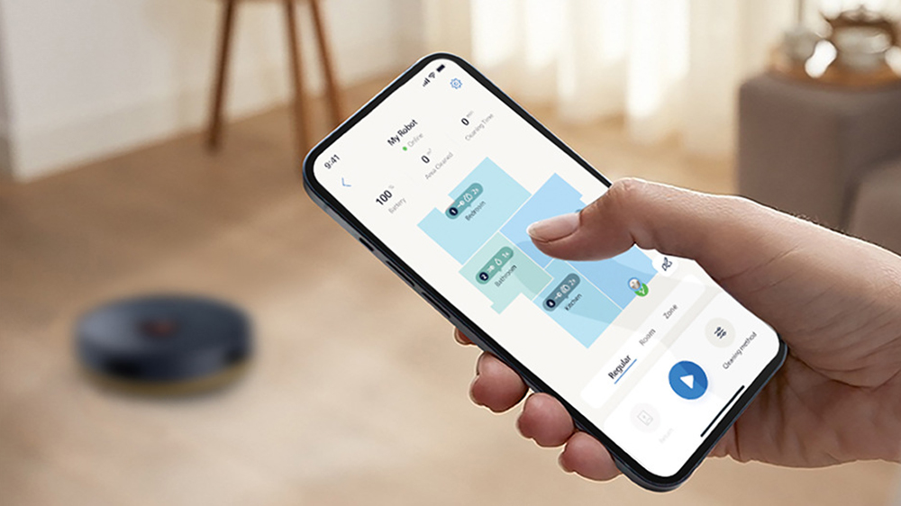 Žena nastavuje úklid místností v aplikaci Philips HomeRun, zatímco na podlaze čeká robotický vysavač Philips Series 2000 XU2100/10_05