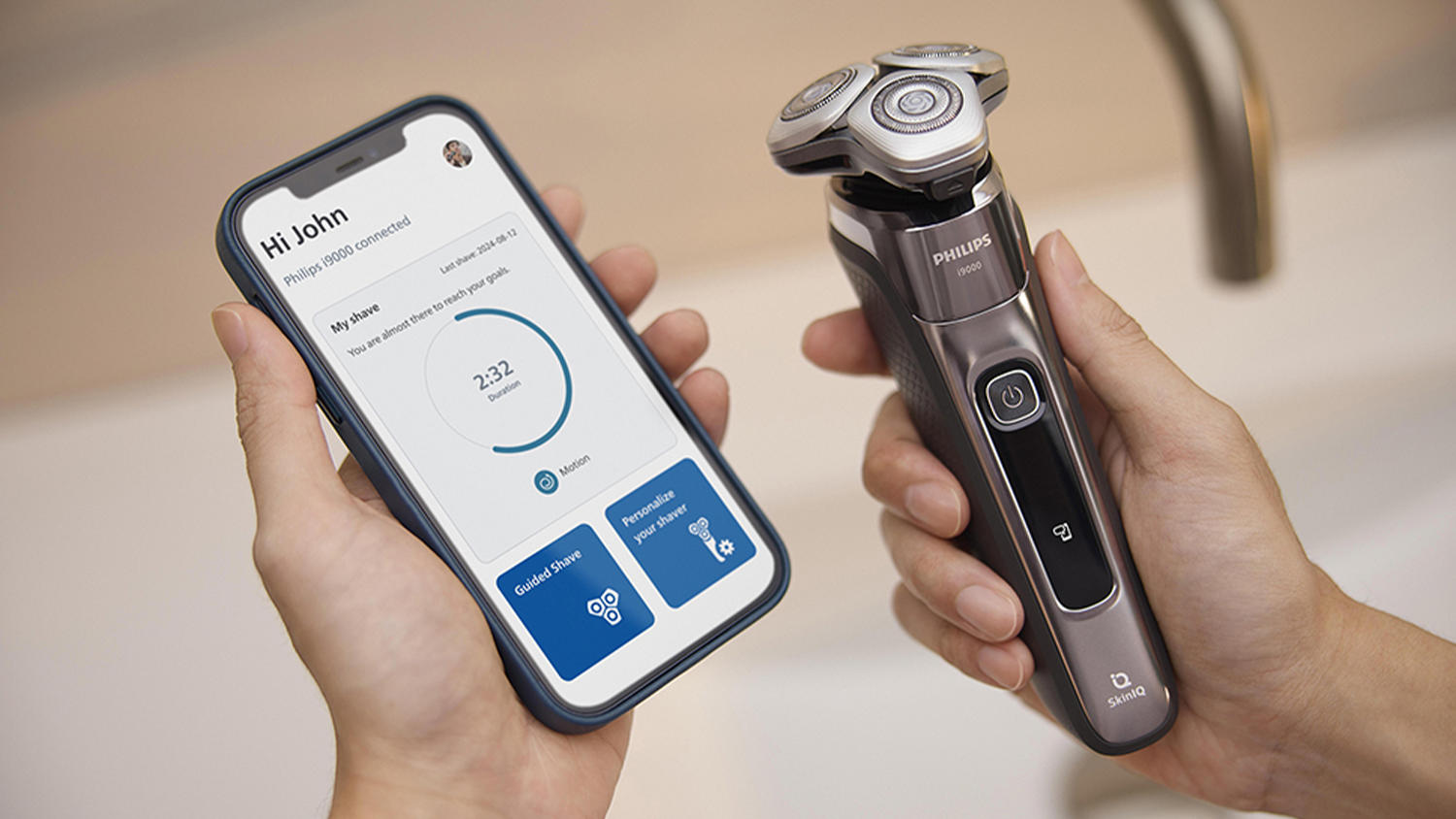 Pohled na Pánský elektrický holicí strojek X9002/10 Philips Series i9000 vedle telefonu se zapnutou mobilní aplikací GroomTribe