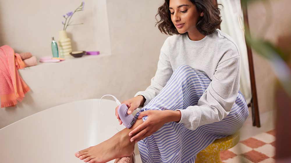 Žena si s &uacute;směvem vytrh&aacute;v&aacute; chloupky na nohou pomoc&iacute; epil&aacute;toru Philips Series 2000 BRE237/00_02