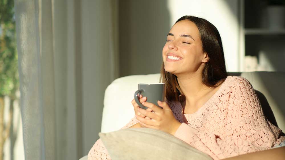 Šťastná žena popíjí kávu doma na gauči_02