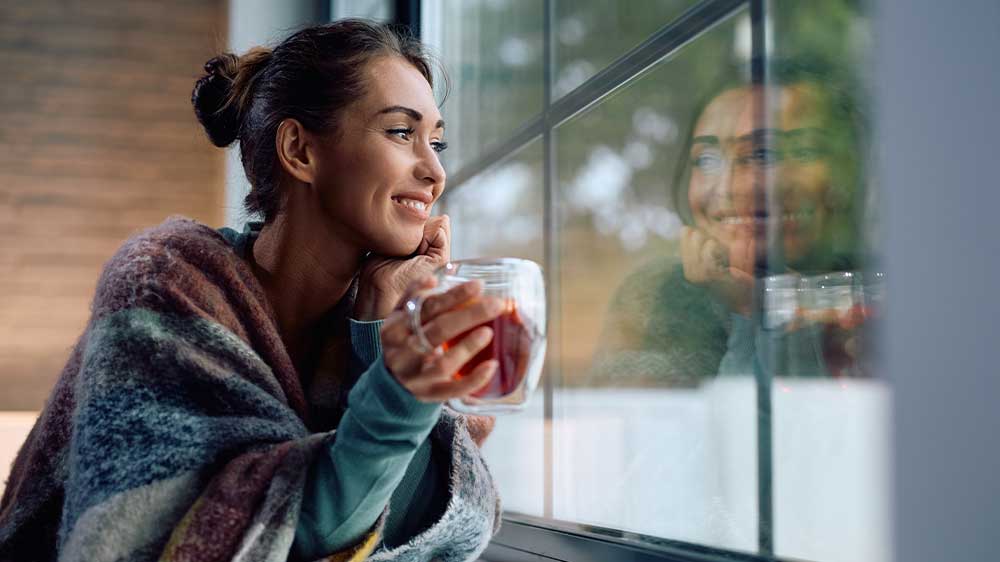 Žena dívající se z okna s šálkem čaje v ruce_02