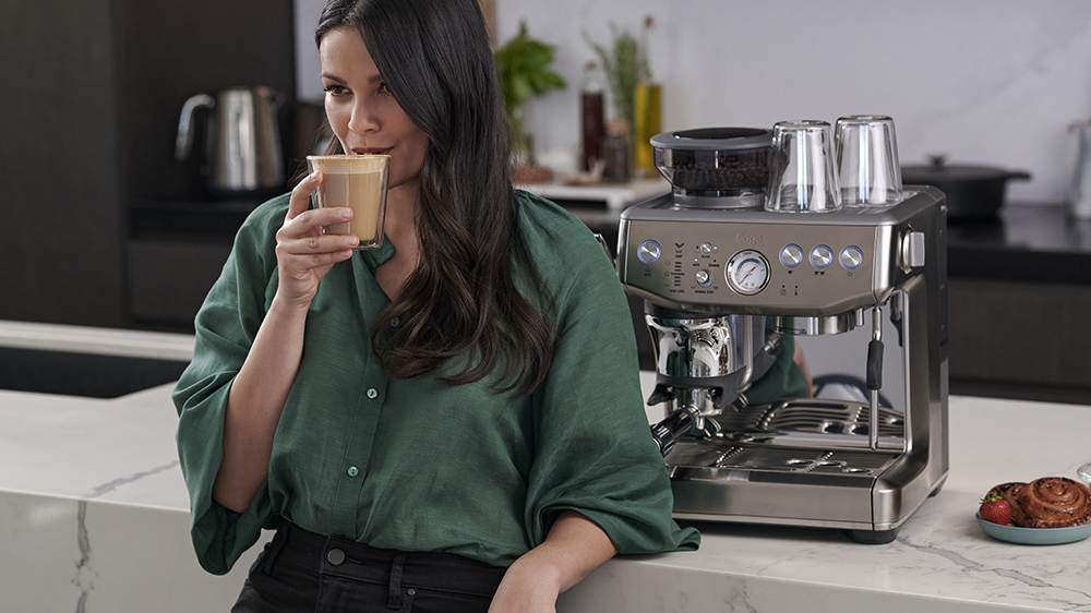 Žena opřená o linku s kávou v ruce vedle kávovaru Sage SES876BTR_02
