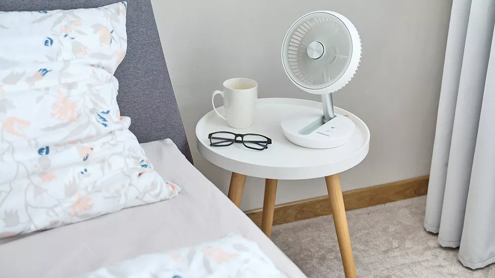 Nočn&iacute; stolek u postele a na něm stoln&iacute; ventil&aacute;tor Sencor SFE 0773WH_05
