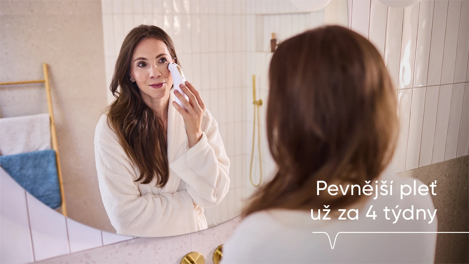 Mlad&aacute; žena stoj&iacute; před zrcadlem a použ&iacute;v&aacute; RF př&iacute;stroj na podporu tvorby kolagenu
