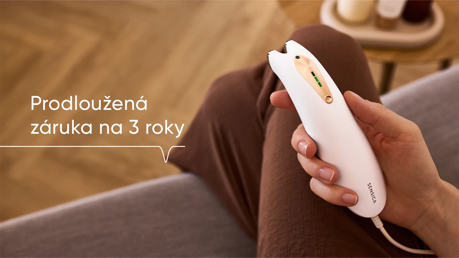 RF př&iacute;stroj Sensica v ruce ženy sed&iacute;c&iacute; na pohovce v ob&yacute;v&aacute;ku