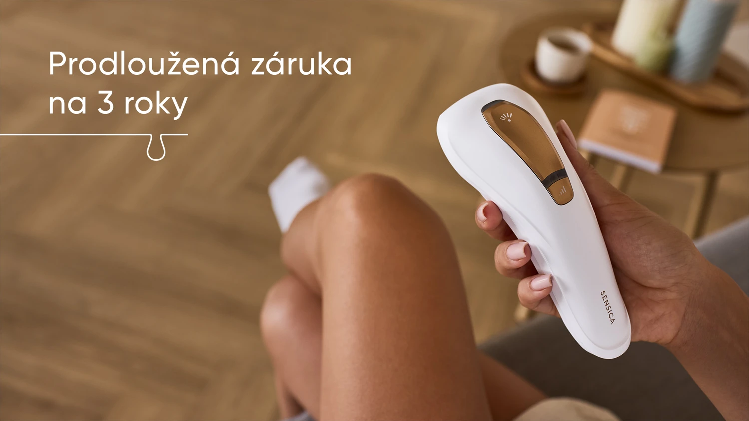IPL epil&aacute;tor Sensica v ruce slečny sed&iacute;c&iacute; na pohovce v ob&yacute;v&aacute;ku