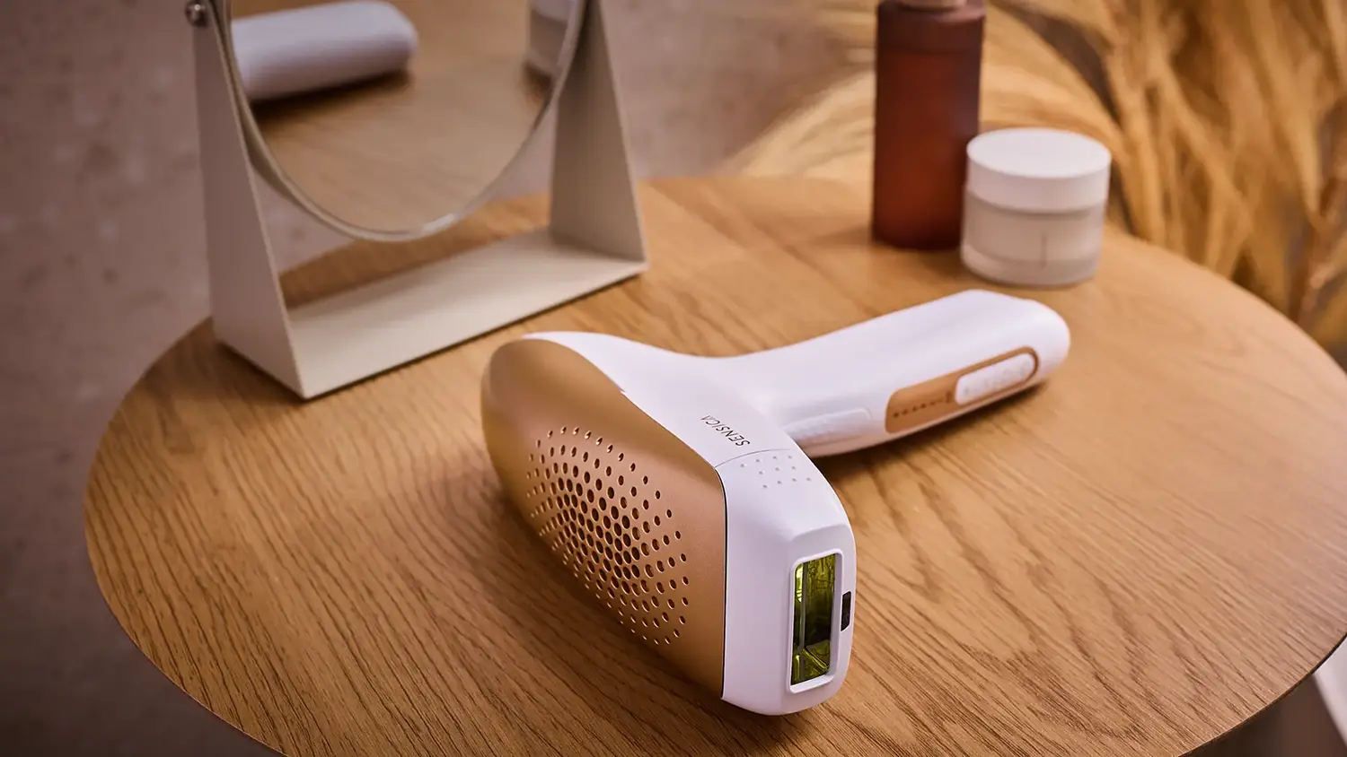 IPL epilátor Sensica Sensilight™ Pro leží na stolíku vedľa zrkadla a kozmetických potrieb