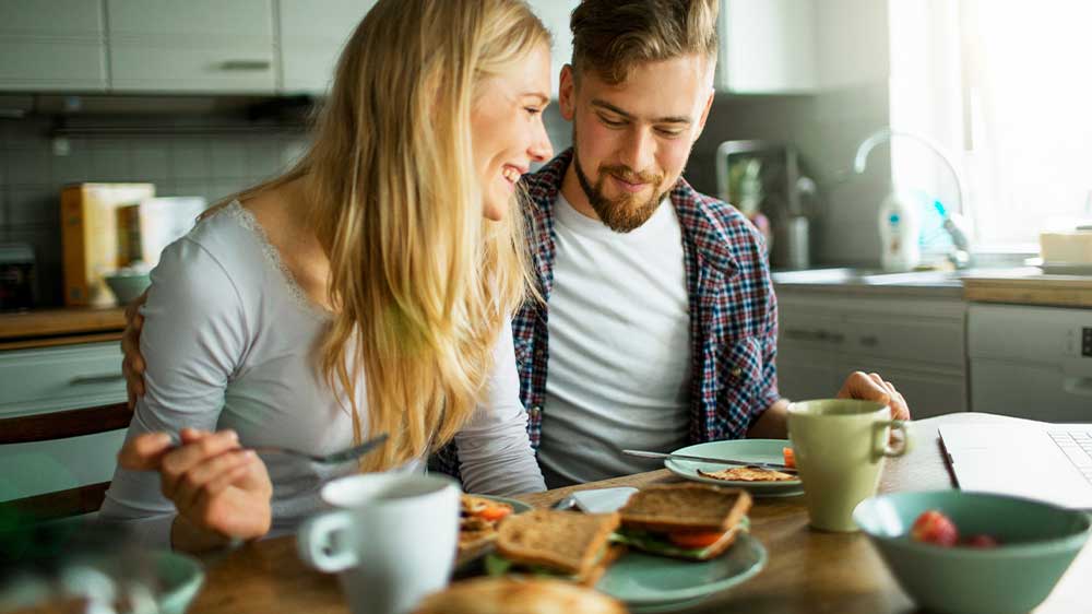 Mladý snídající pár s hrnky horkého nápoje na stole_02