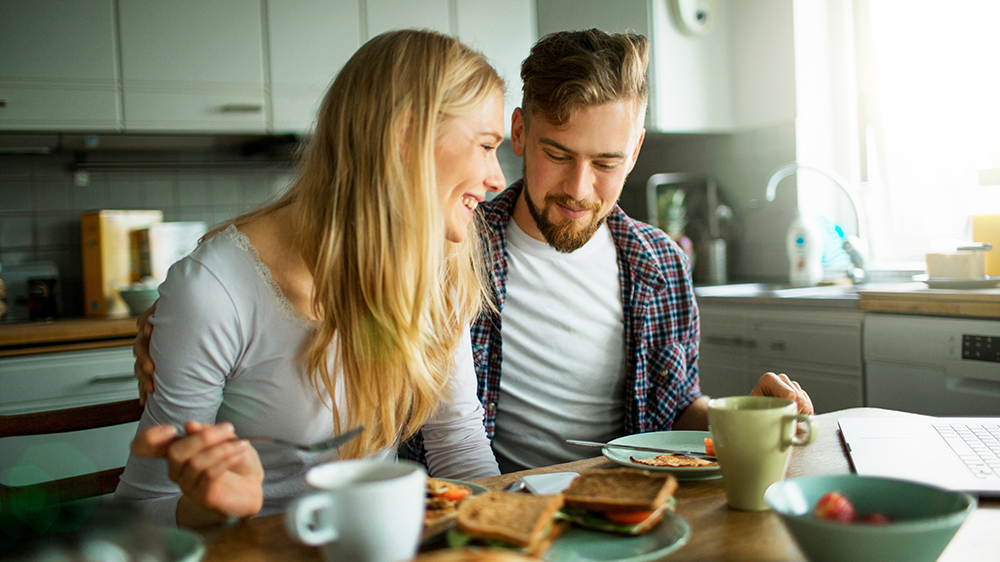 Mladý snídající pár s hrnky horkého nápoje na stole_02