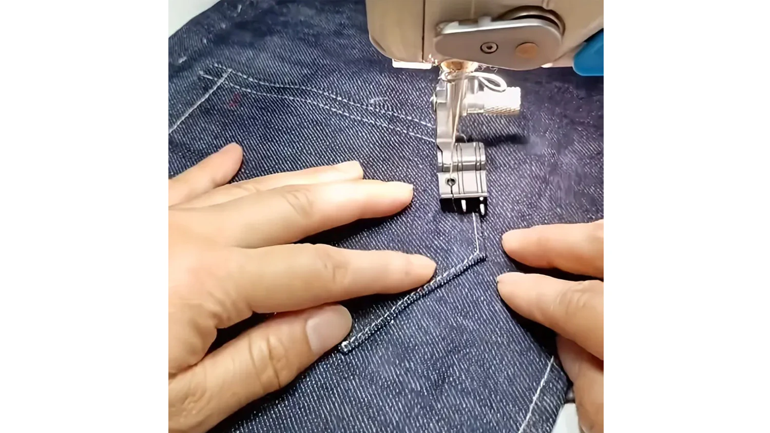 Ruce držící denim látku při práci se šicím strojem