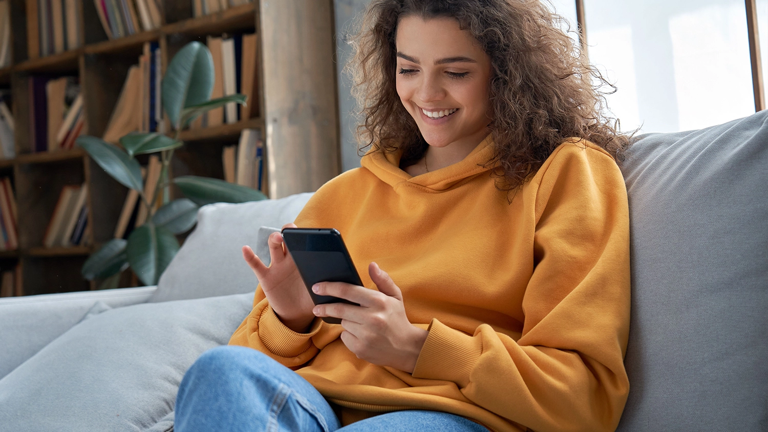 Mlad&aacute; žena na pohovce ovl&aacute;daj&iacute;c&iacute; mobiln&iacute; telefon v ruce