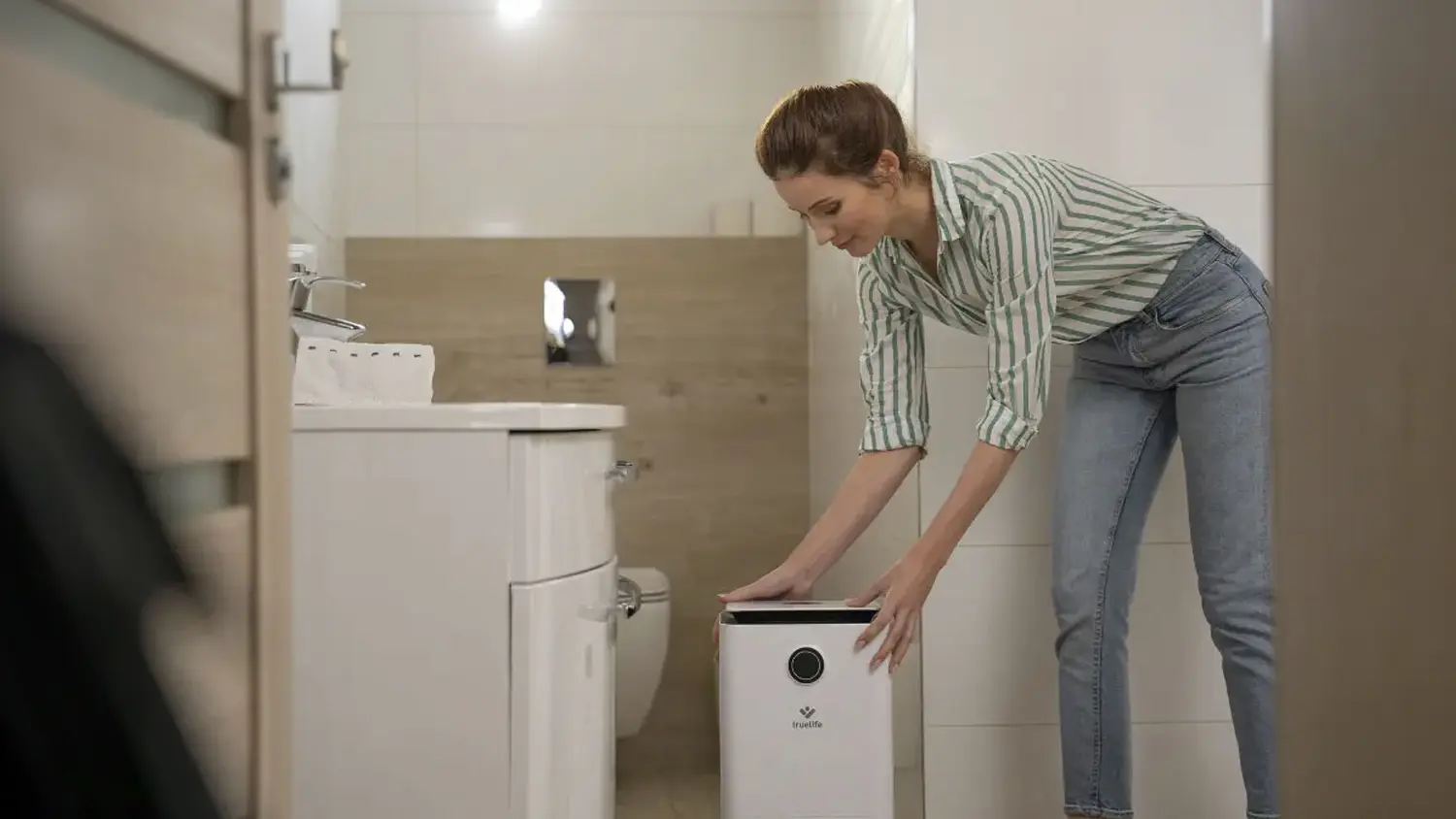 Usmívající se žena umisťuje odvlhčovač vzduchu Truelife DH5 Touch do koupelny