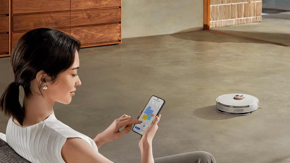 Mladá žena sedící na pohovce a ovládající robotický vysavač Xiaomi S20+ pomocí aplikace v mobilním telefonu_05