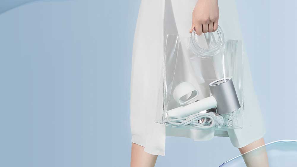 Žena v bílých šatech přenáší fén Xiaomi Water Ionic Hair Dryer H500 EU v průhledné cestovní tašce_03