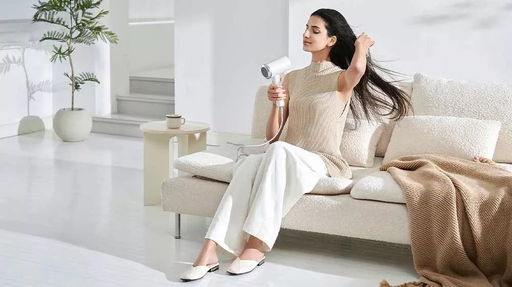 Žena sedí na gauči a suší si dlhé vlasy fénom Xiaomi High-speed Ionic_04