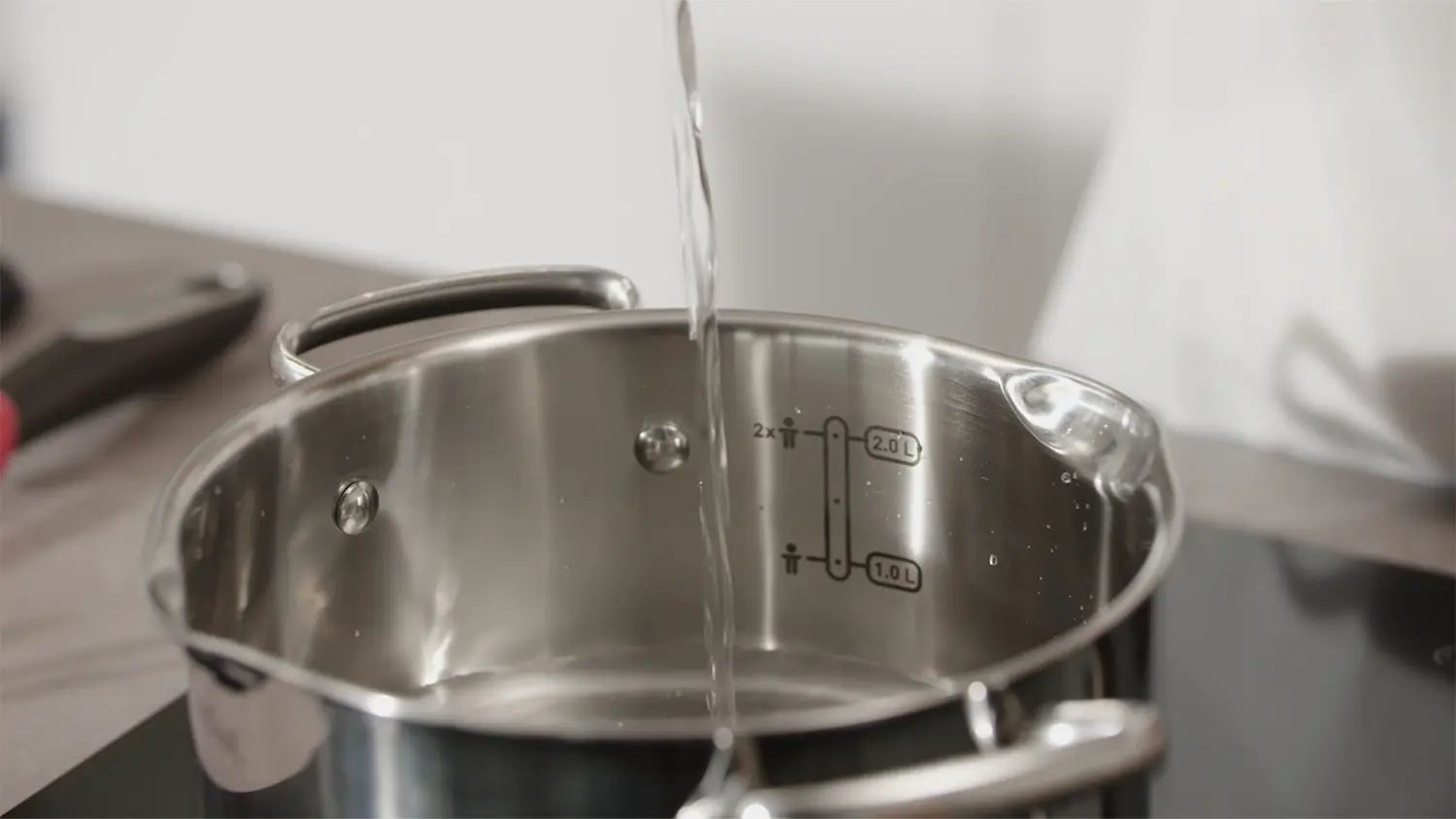 Hrnec s poklic&iacute; Tefal Duetto+ G7194355 18 cm při praktick&eacute;m použit&iacute; v kuchyni s uk&aacute;zkou měrn&yacute;ch rysek.