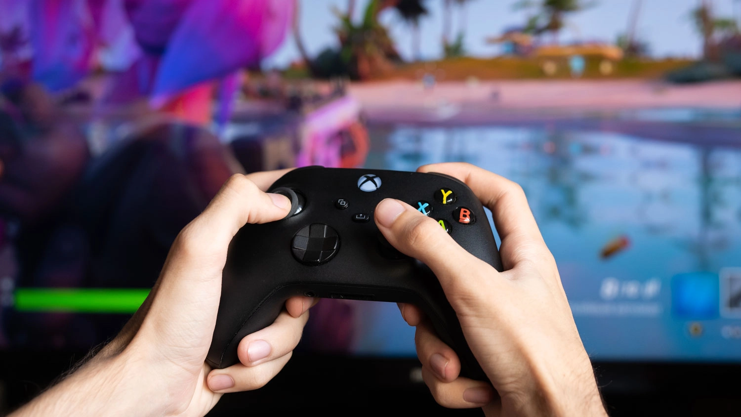Ruce držící černý bezdrátový ovladač Xbox před obrazovkou se spuštěnou videohrou.