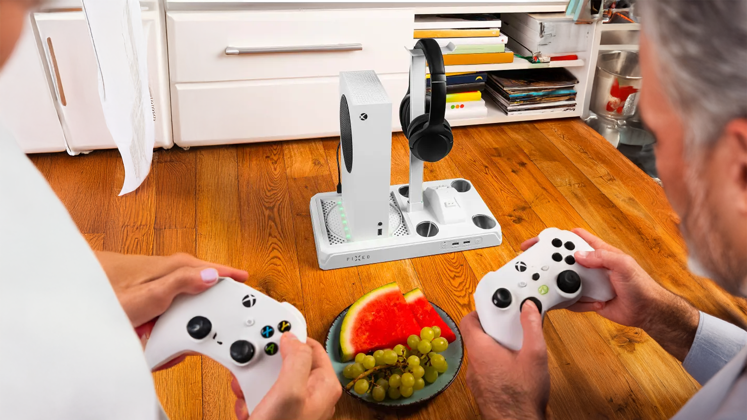 Dva muži hrají na Xboxu a před nimi je na zemi multifunkční stanice Fixed pro Xbox Series X/S bílá