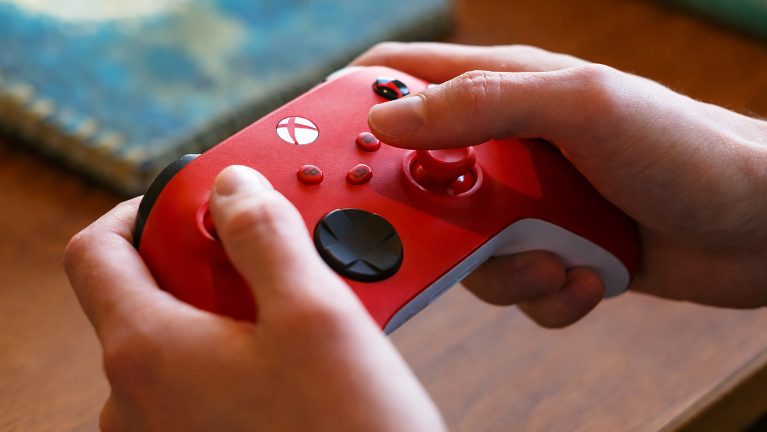 Ruce drž&iacute; červen&yacute; gamepad Microsoft XBOX Series