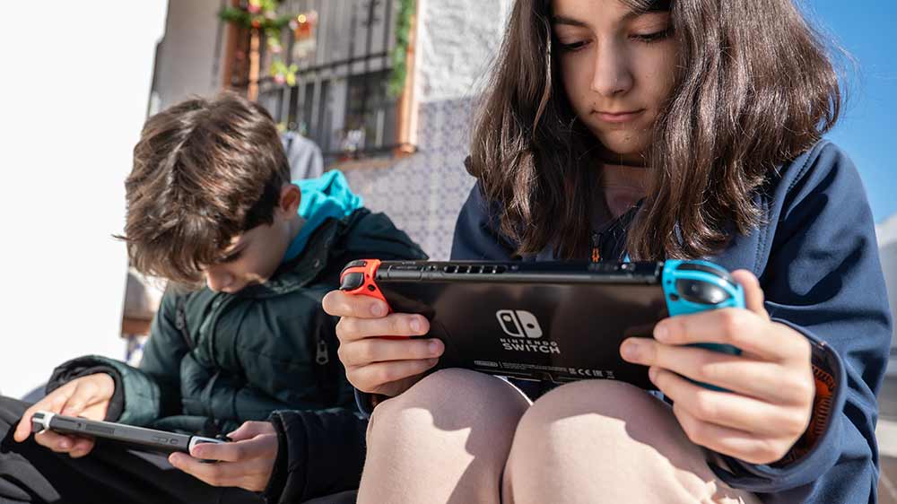 Chlapec a dívka sedící na obrubníku a hrající Nintendo Swith venku_02