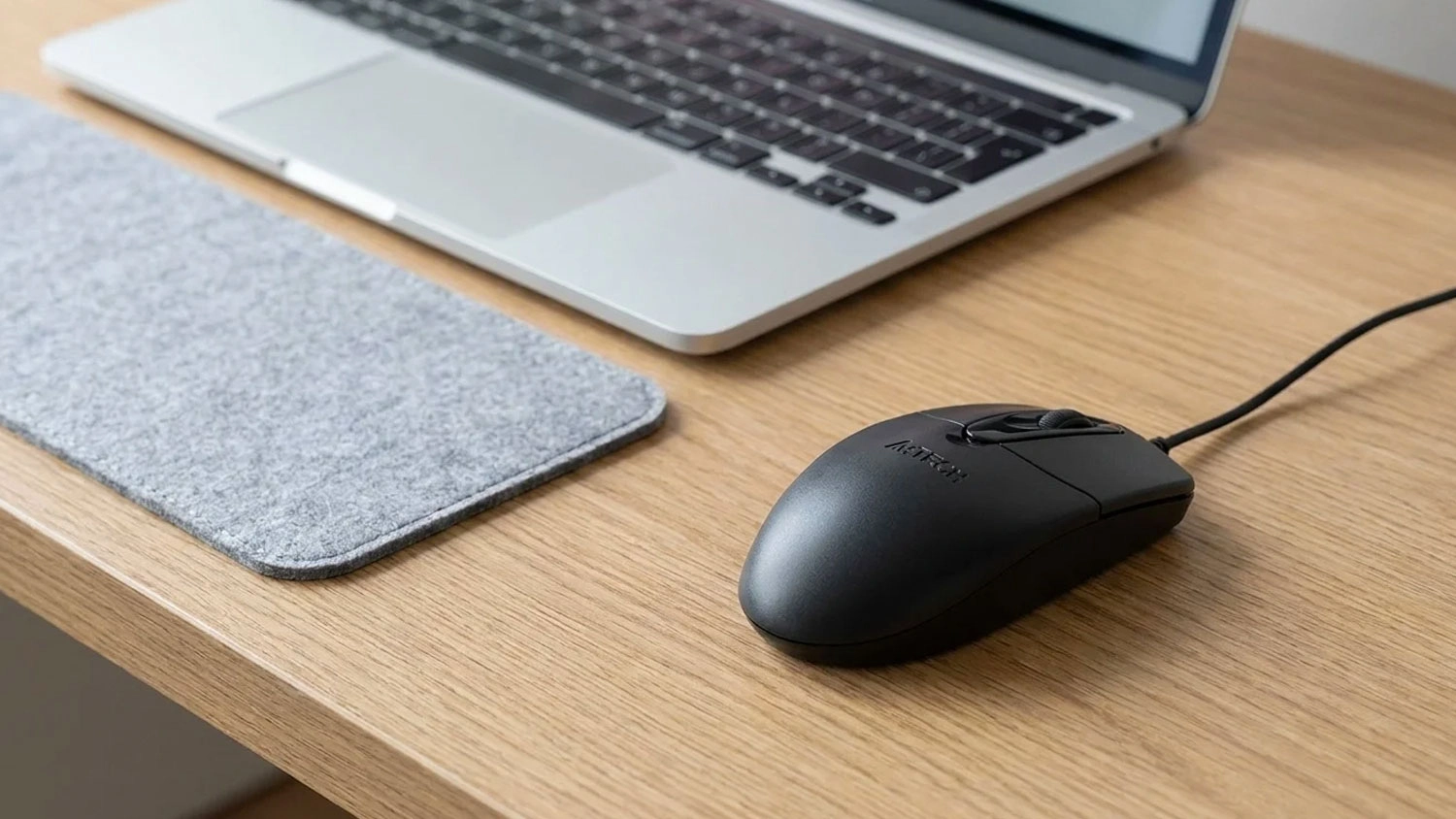 Černá počítačová myš A4TECH OP-720 Black na dřevěném stole vedle otevřeného notebooku.