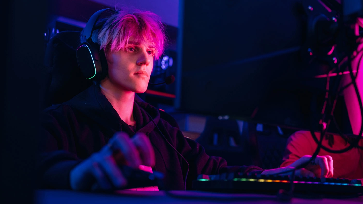 Muž hrá hry na počítači a na stole je podsvietená klávesnica