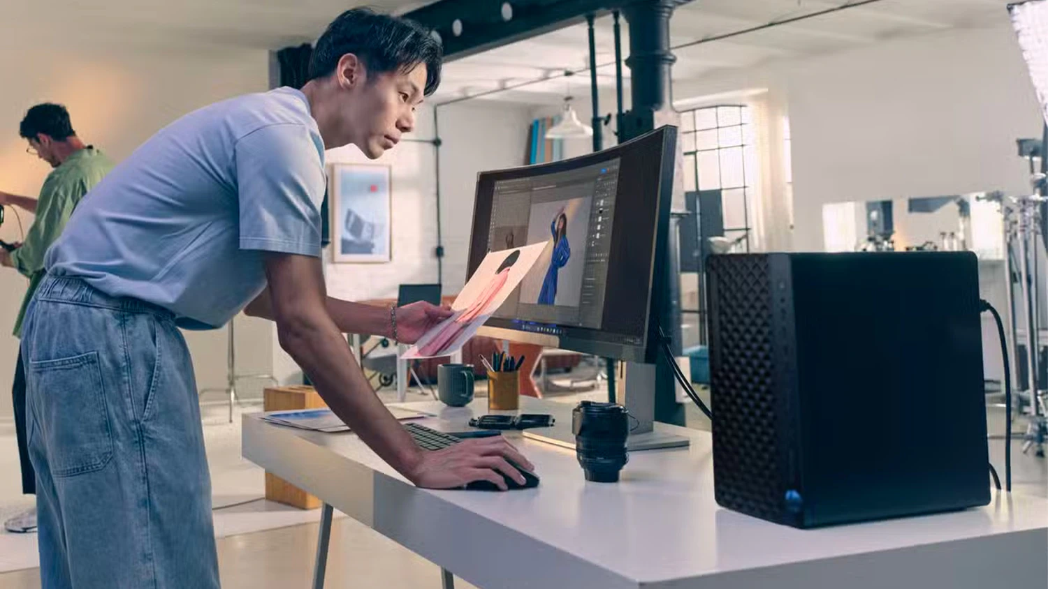 Osoba s fotografi&iacute; v ruce u stolu s monitorem a poč&iacute;tačem HP