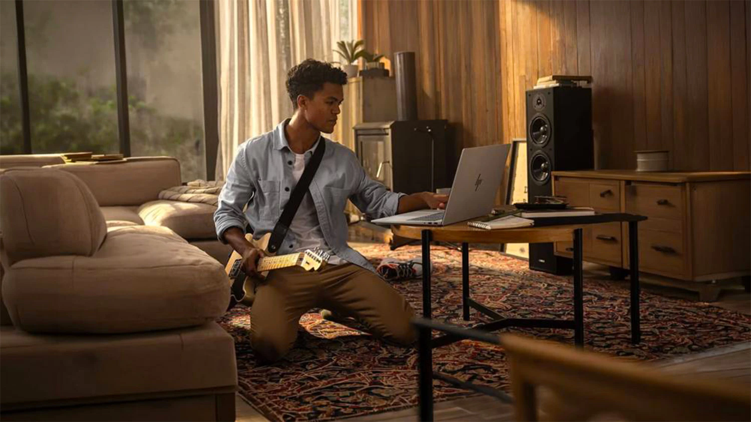 Muž s kytarou na zemi u notebooku HP na stolku