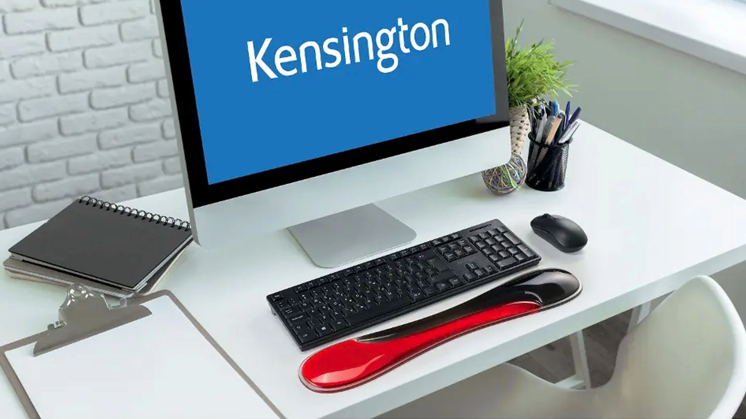Opěrka z&aacute;pěst&iacute; Kensington Slim Duo před kl&aacute;vesnic&iacute; na pracovn&iacute;m stole u poč&iacute;tače.