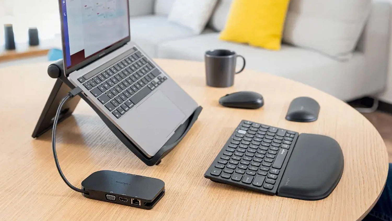Šedá ergonomická opěrka Kensington ErgoSoft přiložená ke kompaktní klávesnici na dřevěném stole vedle notebooku a myši.