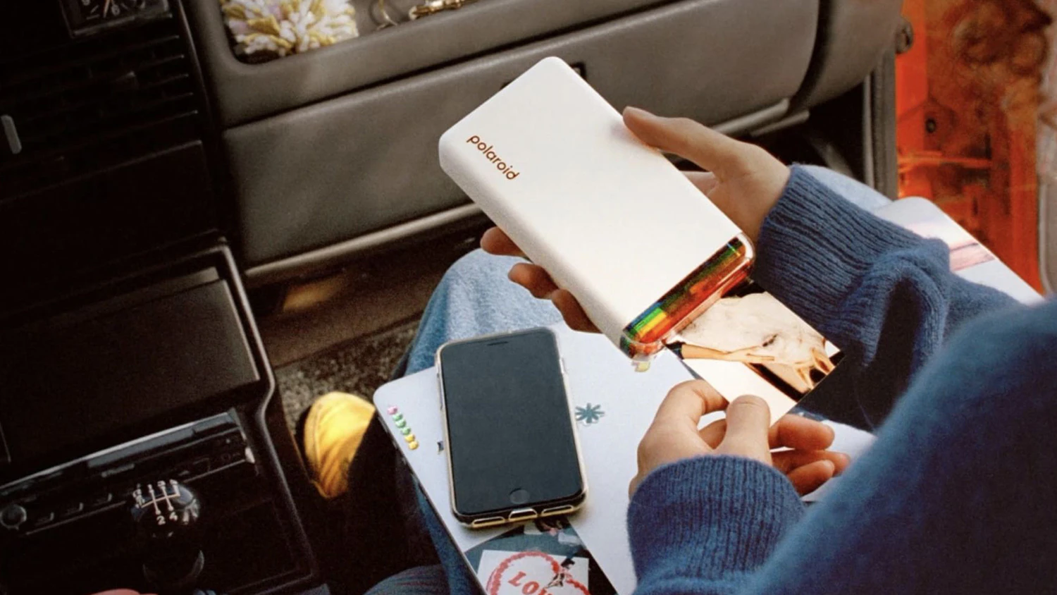Osoba držící tiskárnu Polaroid s fotografiemi v autě