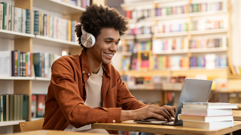 Mladý muž studuje v knihovně na notebooku_03